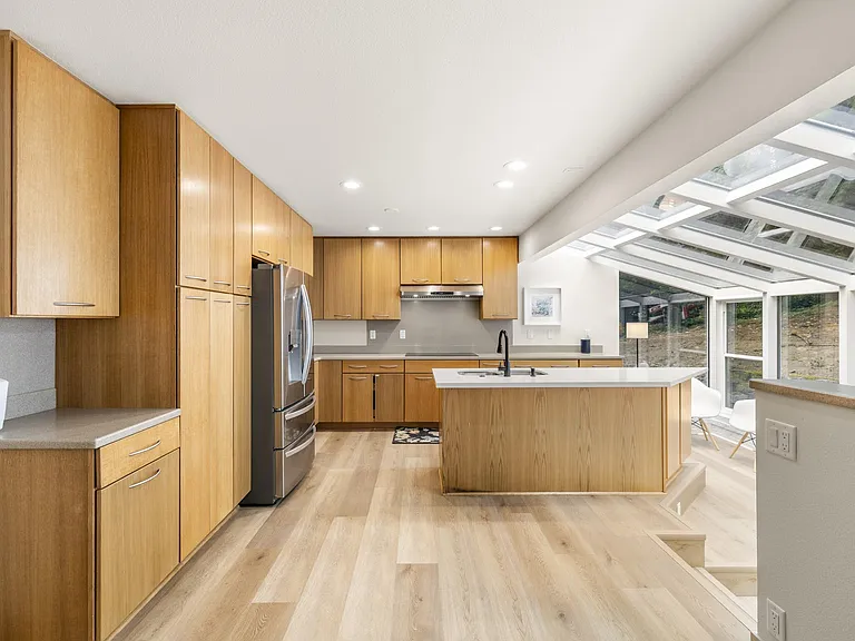 Chef-friendly kitchen with ample cabinetry, stainless-steel fridge, and a large island with sink plus expansive window views.