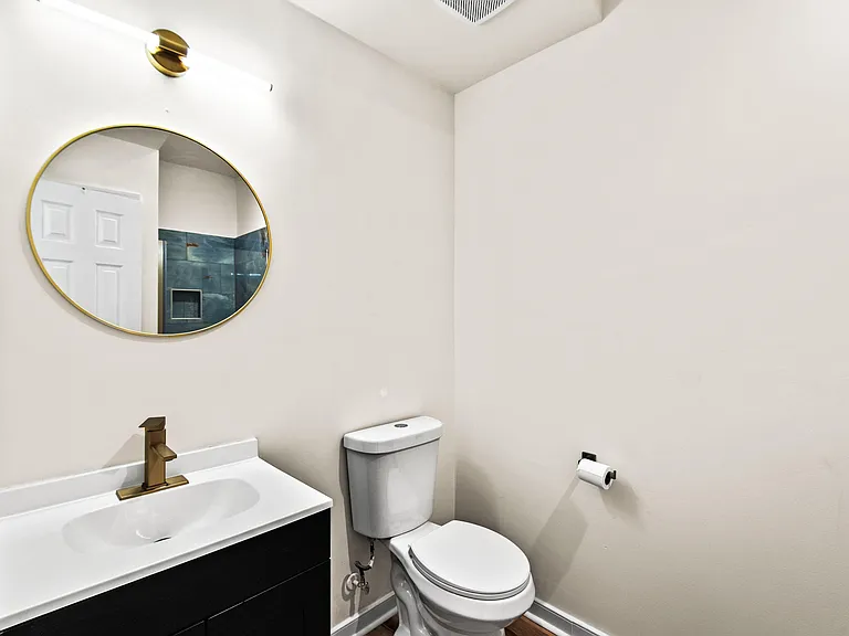 Full bath with a sleek vanity, gold fixtures, and a round mirror.