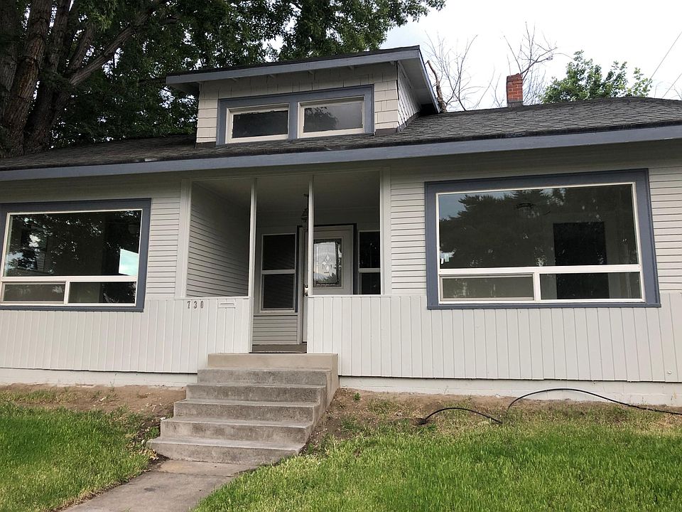 The front of the house - large covered porch, big windows, and grassy yard.