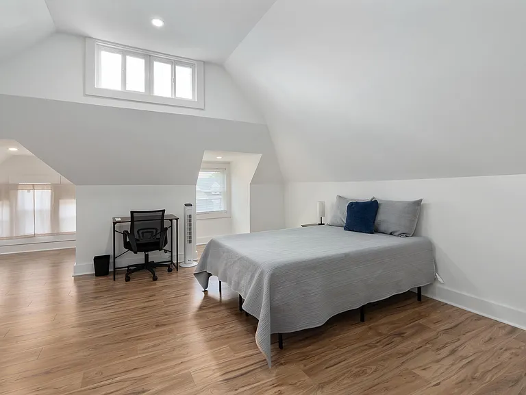 Spacious bedroom with vaulted ceilings, wood-look flooring, and multiple windows plus a dedicated desk workspace.