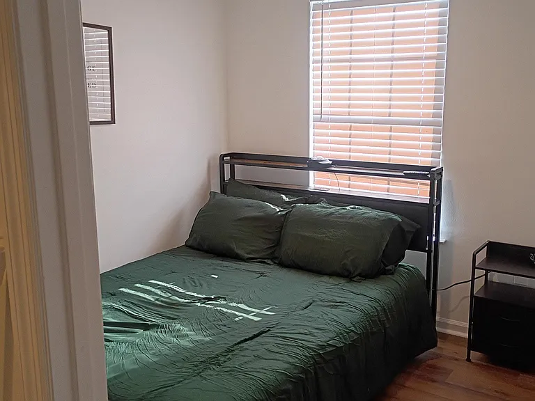 Furnished bedroom featuring a queen-size bed, nightstand, and a window with blinds for light and privacy.