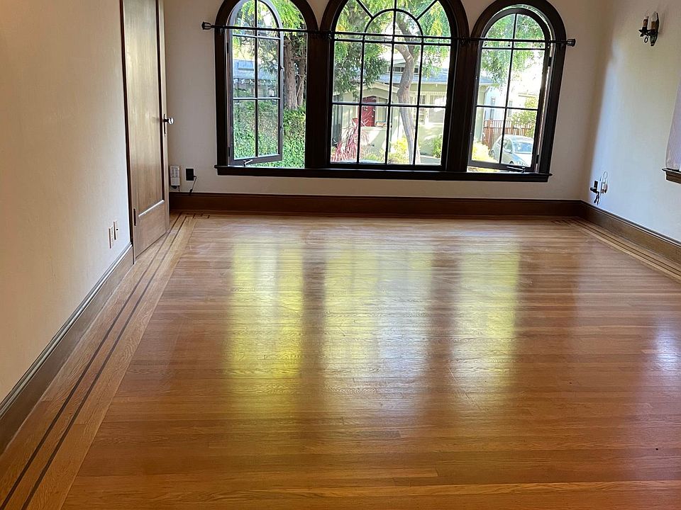 Large living room with hardwood floors and windows that open to tree lined street.