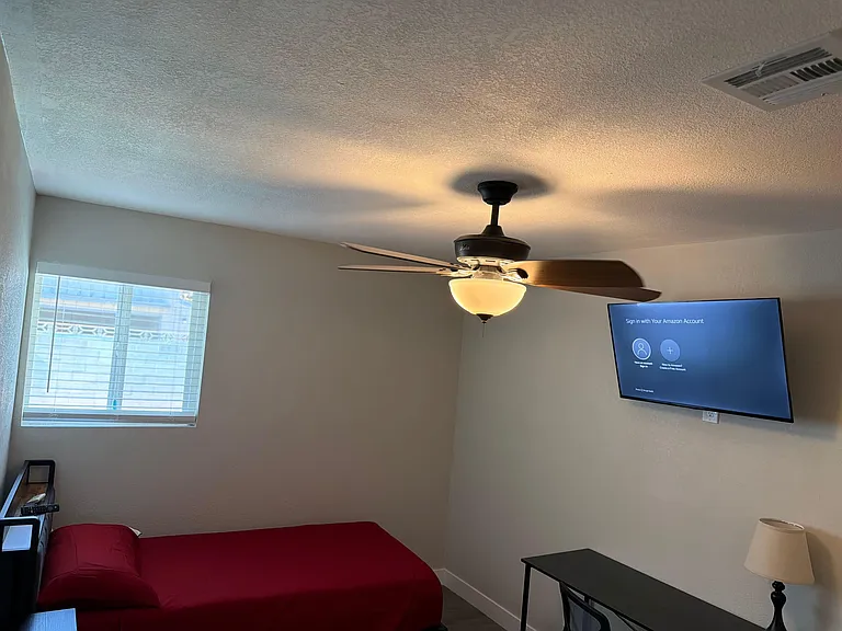 Private bedroom with a ceiling fan/light, window with blinds, and wall-mounted TV for easy relaxing and streaming.