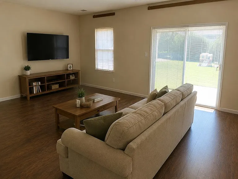 Open living area with wood-look floors, a comfortable seating setup, and sliding glass doors leading to the backyard.