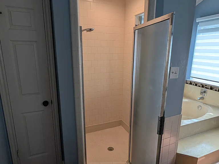 The shower is spacious with a hand-held shower head and a combination of natural and overhead light.