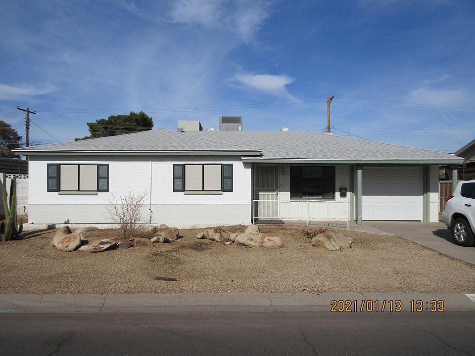 Front of home features covered entry, sun screens, security door, and desert landscape.