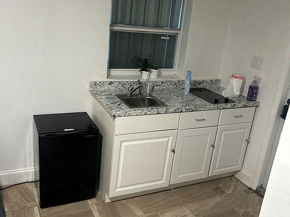 Compact kitchenette with granite-look counters, sink, base cabinetry, and space for a mini fridge.