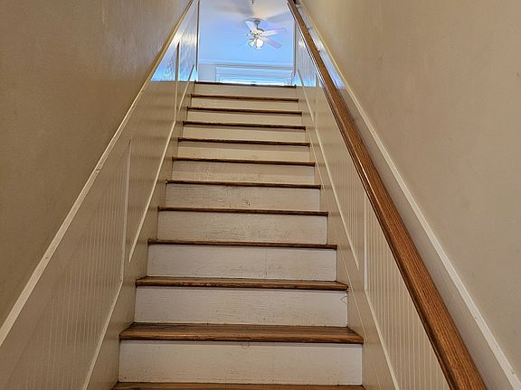 Elegant wood staircase with matching handrail and white trim leading from the front entry to the main living level, with natural light pouring in from the upper window.