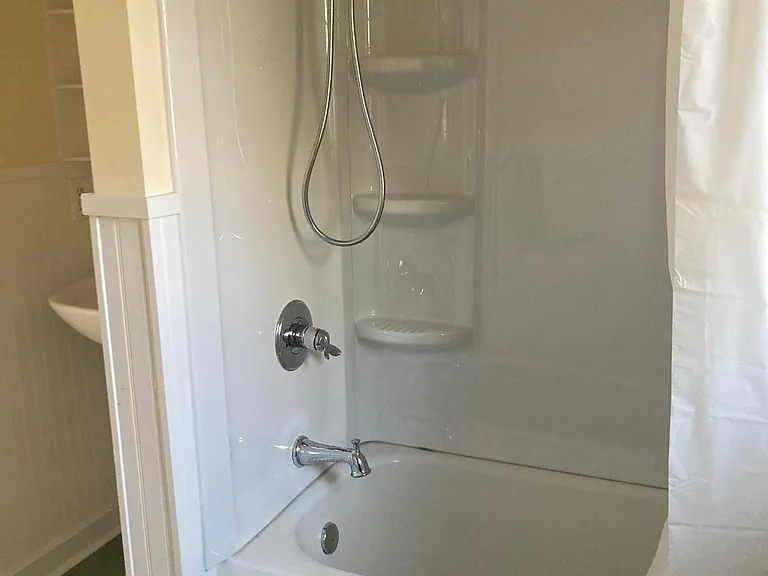 The newly remodeled bathroom features a vintage tub and a brand new shower surround with plenty of storage and a handheld shower head option.