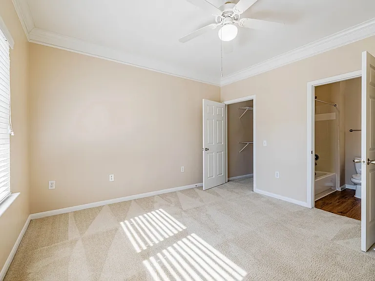 Bright and inviting bedroom with plush carpet, large window for natural light, ceiling fan, and bathroom. Bright and inviting bedroom with plush carpet, large window for natural light, ceiling fan, and bathroom.