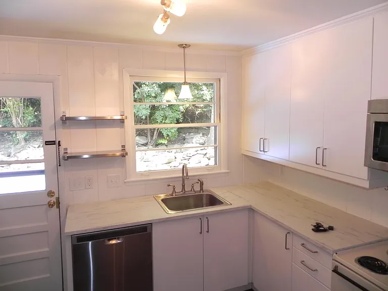 kitchen with dishwasher, microwave, stove. View through windows to backyard.