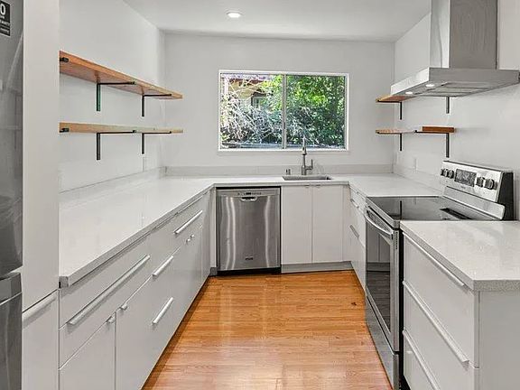 This bright, modern kitchen is a cook's dream _ sleek quartz countertops, stainless steel appliances, and plenty of prep space make it perfect for everyday meals or dinner parties. The open shelving adds allows for plenty of storage area.