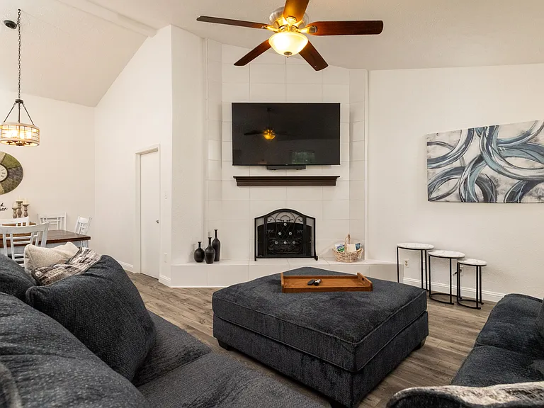 Open and inviting living room featuring a cozy couch, oversized ottoman, ceiling fan for added comfort, flat-screen Roku TV, and a beautiful indoor fireplace that adds both warmth and character.