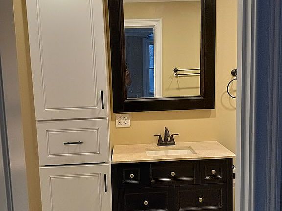 Bathroom features plenty of storage. Featuring a built-in cabinet spanning from floor to ceiling with deep shelves and drawers. The bottom is perfect for a hamper. the drawer and shelves above that offer plenty of storage for towels or other items. A modern bathroom cabinet for the sink features a marble like top with a built-in undermount porcelain sink and oil rubbed bronze faucet. That sits below a oversized custom medicine cabinet