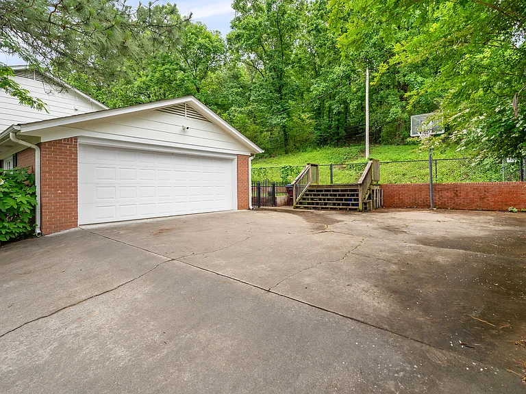 2.5 car, extra long garage, hardwired for EV charging with charger installed (can be negotiated with lease). Stairs lead to fenced, wooded backyard with a firepit. The top of the driveway holds 3 parked cars and features a basketball hoop.