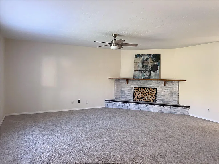 Unfurnished living room with ceiling fan, carpet flooring, and a brick fireplace
