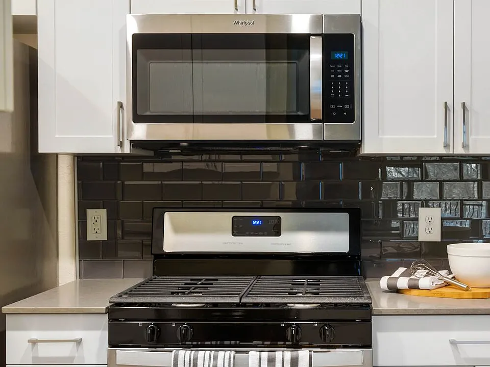 Renovated Package I kitchen with white cabinetry, grey quartz countertops, glass tile backsplash, and stainless steel appliances, and hard surface plank flooring