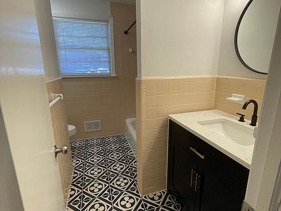 Full bathroom with shower/tub combo, new tile, toilet, fixtures, lighting and vanity. Features original 1950's tile and new geometric tile.