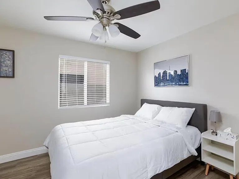 Well-appointed bedroom with a ceiling fan, window with blinds, and space for a full/queen bed with bedside table.