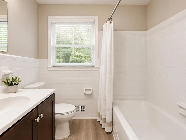 Clean full bath with a tub/shower combo, tiled surround, and a wide vanity counter plus a window for natural light.