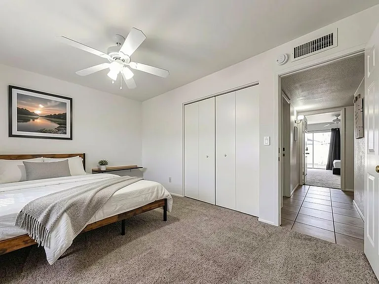 Spacious bedroom with a ceiling fan, plush carpet, and a large sliding-door closet for convenient storage.