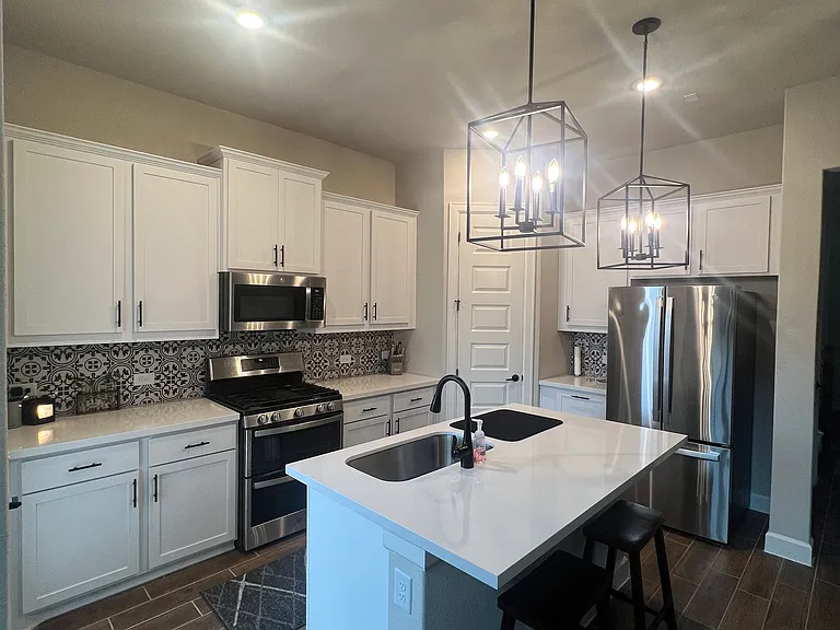 Bright white kitchen with stunning backsplash, brand-new appliances, elegant light fixtures, and abundant storage.