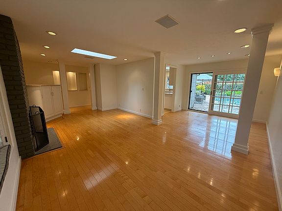 Bright, airy living room features a bay window, skylight, wood-burning fireplace, hardwood flooring and a sliding patio door that opens to a resort-like backyard with sparkling pool and gas grille.