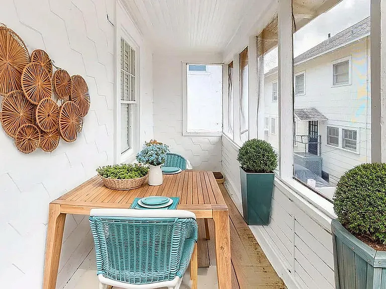 Charming sunlit porch with a stylish wooden dining table, cozy turquoise chairs, and vibrant potted plants, perfect for relaxing dining.