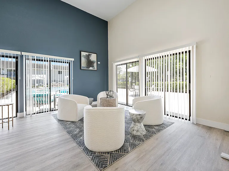 Bright and modern living area with sleek white chairs and expansive windows overlooking a pool oasis.