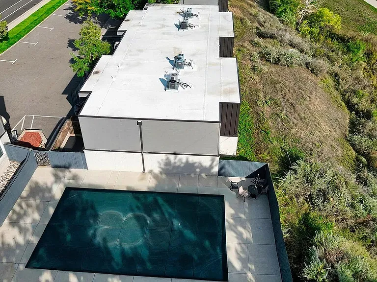 Aerial view of modern apartment complex featuring lush greenery and a sleek swimming pool area.