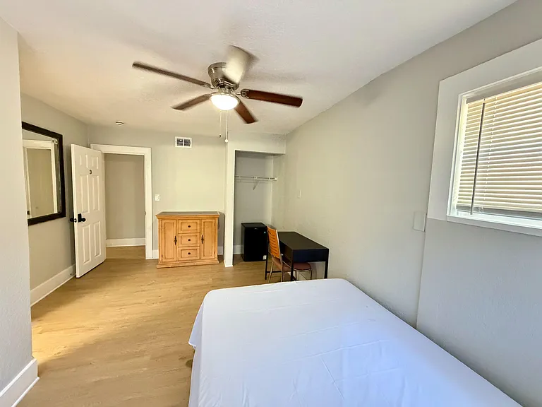 Private bedroom with ceiling fan, window blinds, open closet storage, and a dedicated desk area for work or study.