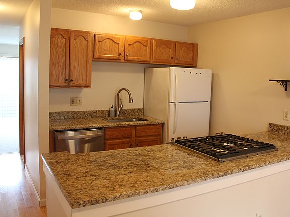 Kitchen with granite countertop, dishwasher and gas stove. Real hardwood floors lead into the living room.