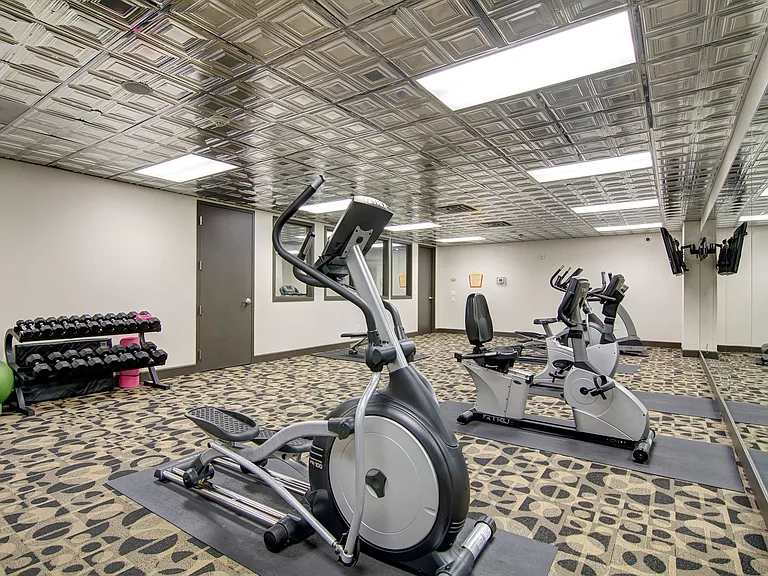 A large room with treadmills, bikes, ellipticals, dumbbells and two flat screen TVs