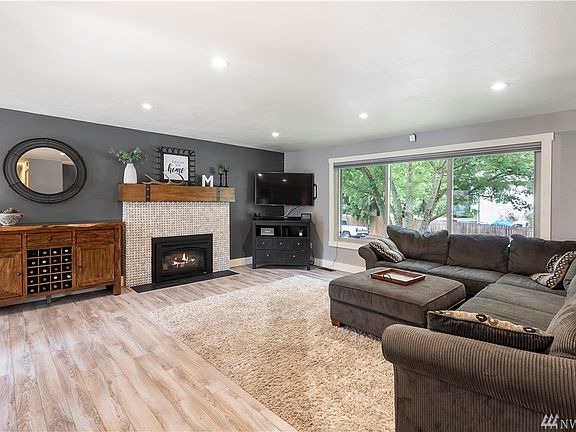 Spacious living room with a stunning gas fireplace as the focal point with ornate tile and a rustic mantle. 