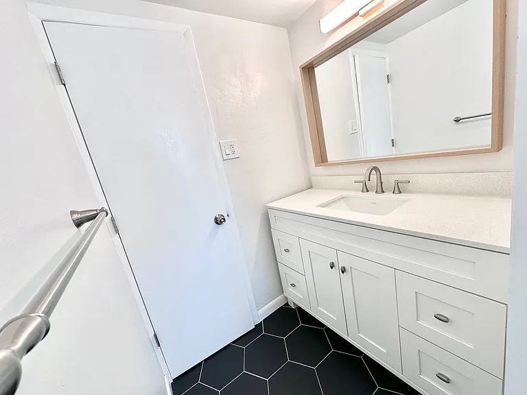 Sleek bathroom featuring a stylish vanity with a large mirror and hexagonal black tile flooring. Sleek bathroom featuring a stylish vanity with a large mirror and hexagonal black tile flooring.