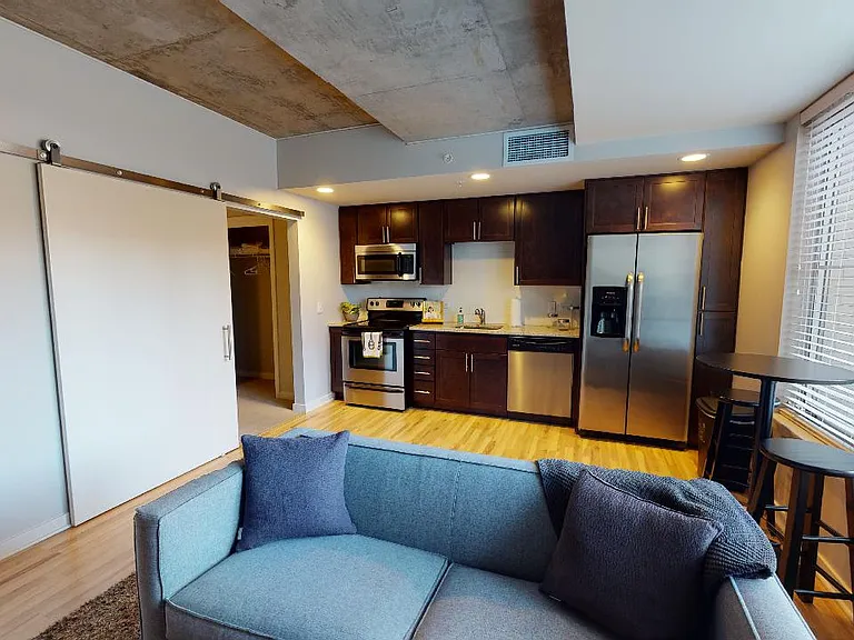 Apartment kitchen with stainless steel appliances, dining and living room with wood-style flooring.