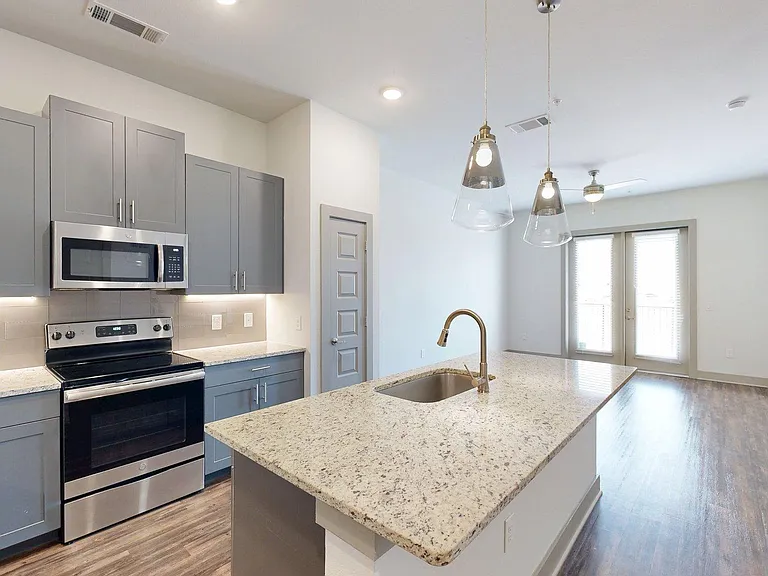 Apartment Kitchen with Stainless Steel Appliances, Dining and Living Room with Wood Style Flooring.