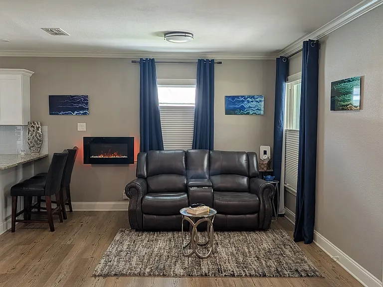 Shared Space-The fully furnished living room features a comfortable loveseat with dual recliners and an electric fireplace that offers both adjustable heating and ambient lighting.