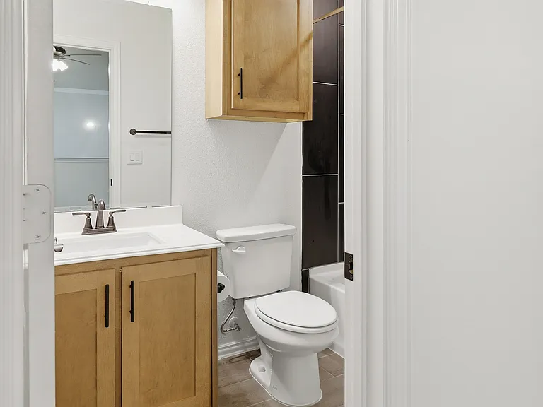 Bathroom featuring a wood-finish vanity with a white countertop, coordinating wall-mounted mirror, and a toilet
