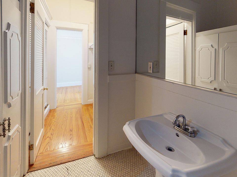 Bathroom with sink, large mirror, hexagonal tiles, leading to hallway with wooden floor