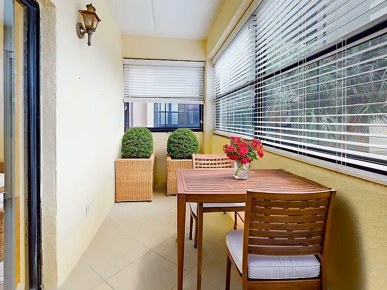 Charming sunlit balcony with a cozy seating area, wooden dining table, and vibrant greenery, perfect for relaxing afternoons.
