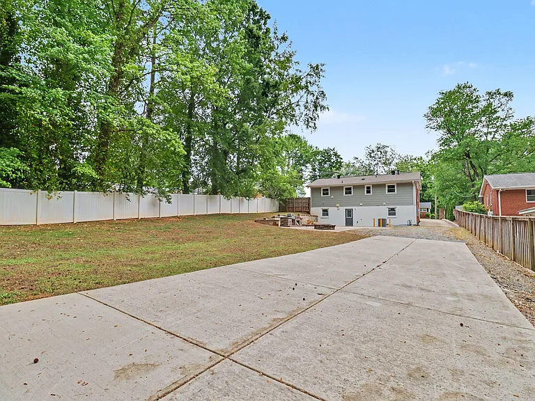 Large fenced backyard with a wide concrete driveway and mature trees, offering plenty of space for parking outdoor use.