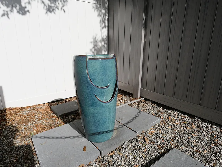 Elegant outdoor space featuring a modern blue ceramic fountain, surrounded by a white fence and stone tiles, creating a serene ambiance.