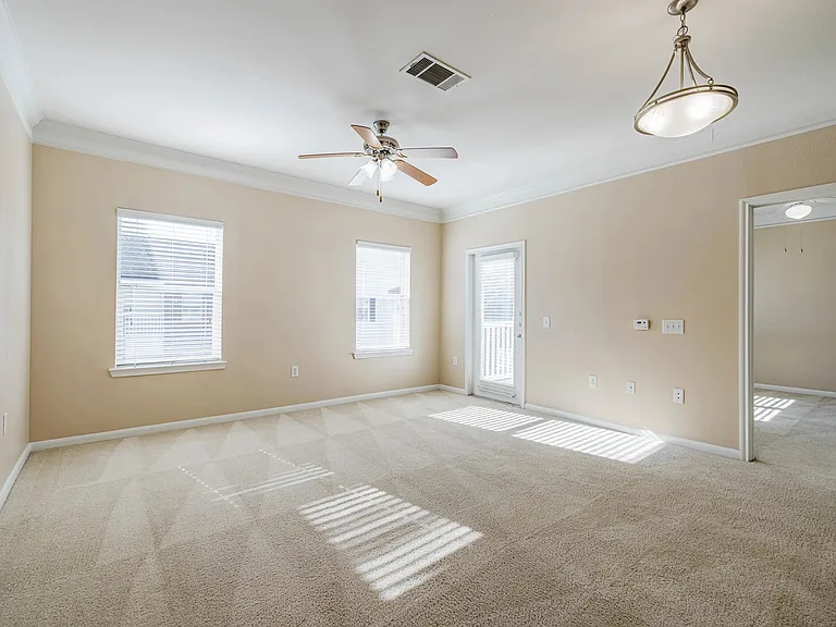 Bright and airy living room with plush carpeting, ceiling fan, and ample natural light from large windows and a glass door. Bright and airy living room with plush carpeting, ceiling fan, and ample natural light from large windows and a glass door.