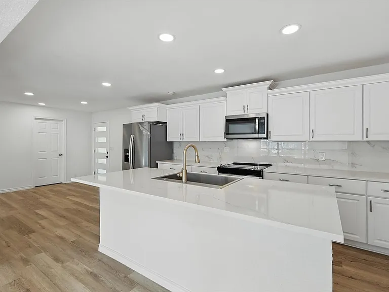 Kitchen with stainless steel appliances, a sink, a kitchen island with sink, recessed lighting, and white cabinetry