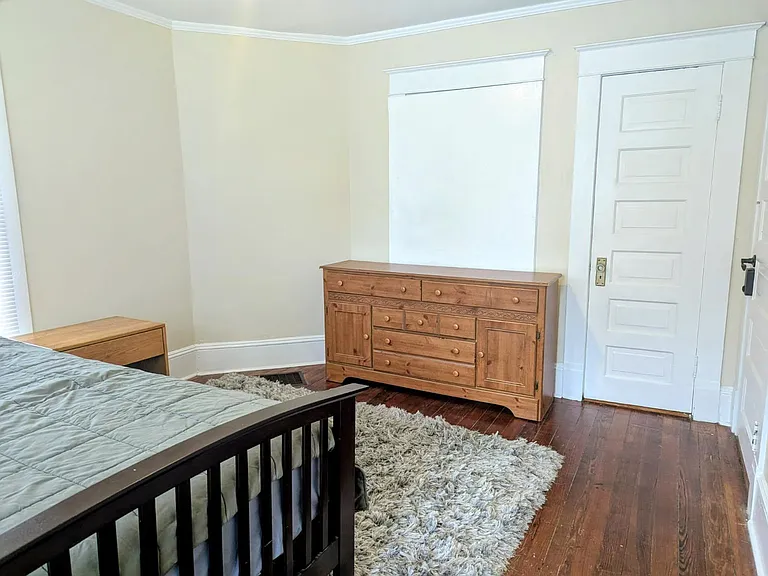 Bedroom with hardwood floors, window for natural light, and dresser storage, plus space for a bed and side table.