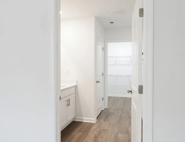 Doorway from the primary bedroom into the private bath and closet wing. Wood-look flooring transitions into the bath area. Multiple doors provide access to a walk-in closet and bathroom.
