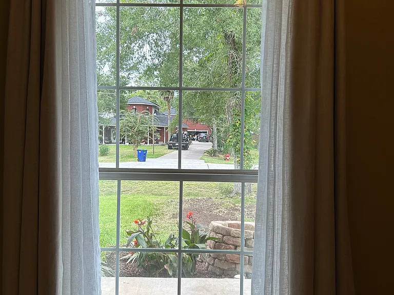 view from front bedroom overlooks flower bed with stone wishing well and beautiful home across the street