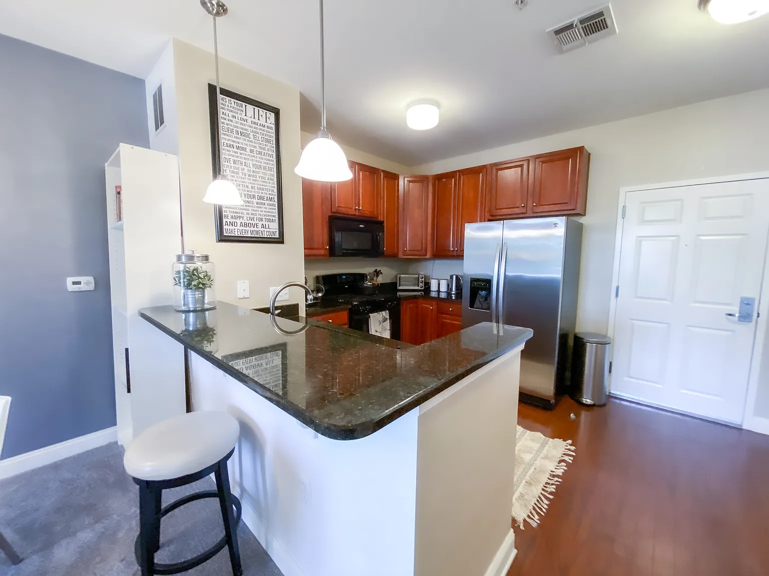 Open kitchen with granite breakfast bar, pendant lighting and stainless steel refrigerator