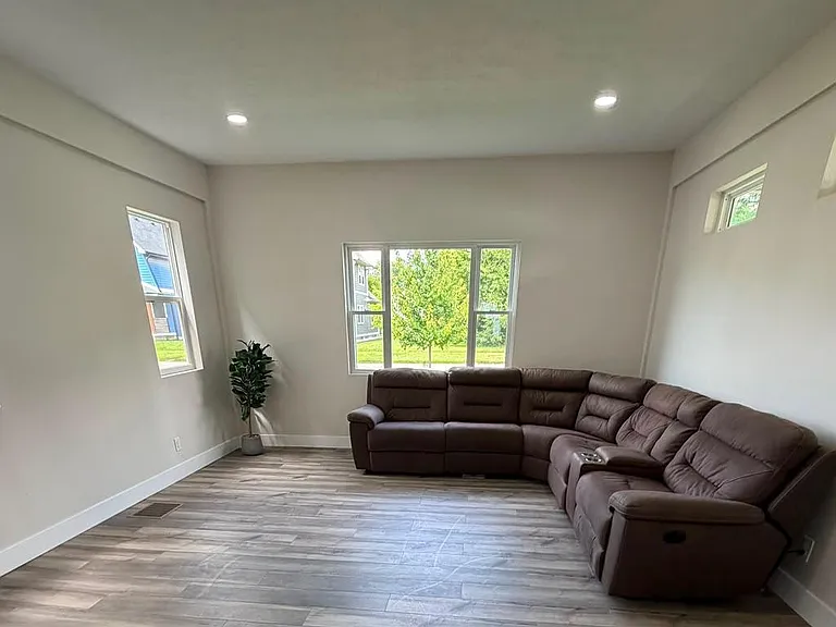 Open living room with recessed lighting, wood-look floors, and a large sectional seating area by multiple windows.